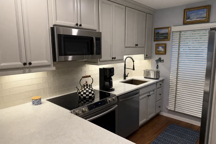 Starting photo of a kitchen, clutter removed: gray cabinets, white counters and a subway tile backsplash.