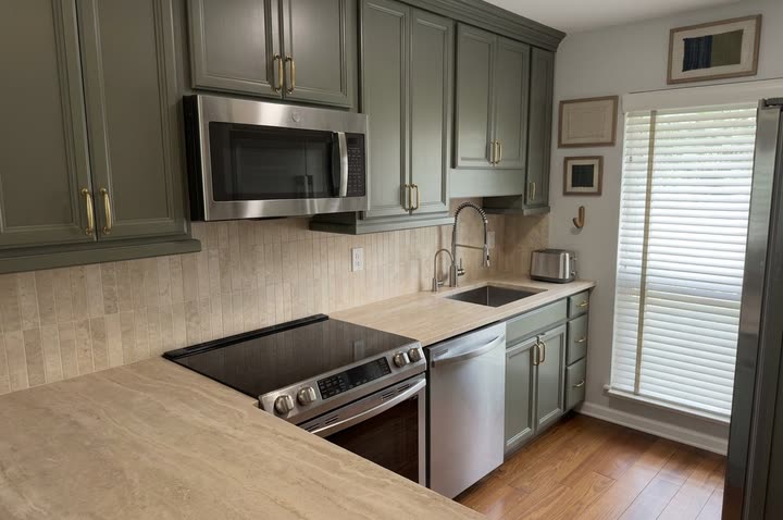 The Renovations Lite concept for the same kitchen: sage green cabinets with brass pulls, stone-look counters and a tall stone tile backsplash.