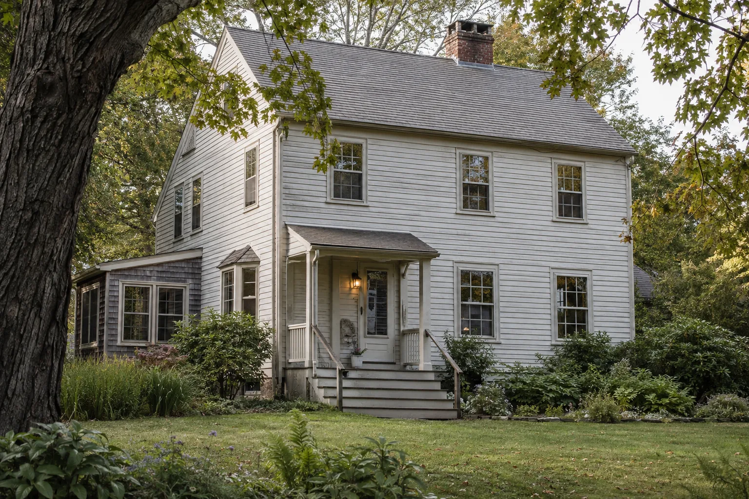 An older white house framed by mature trees and a garden